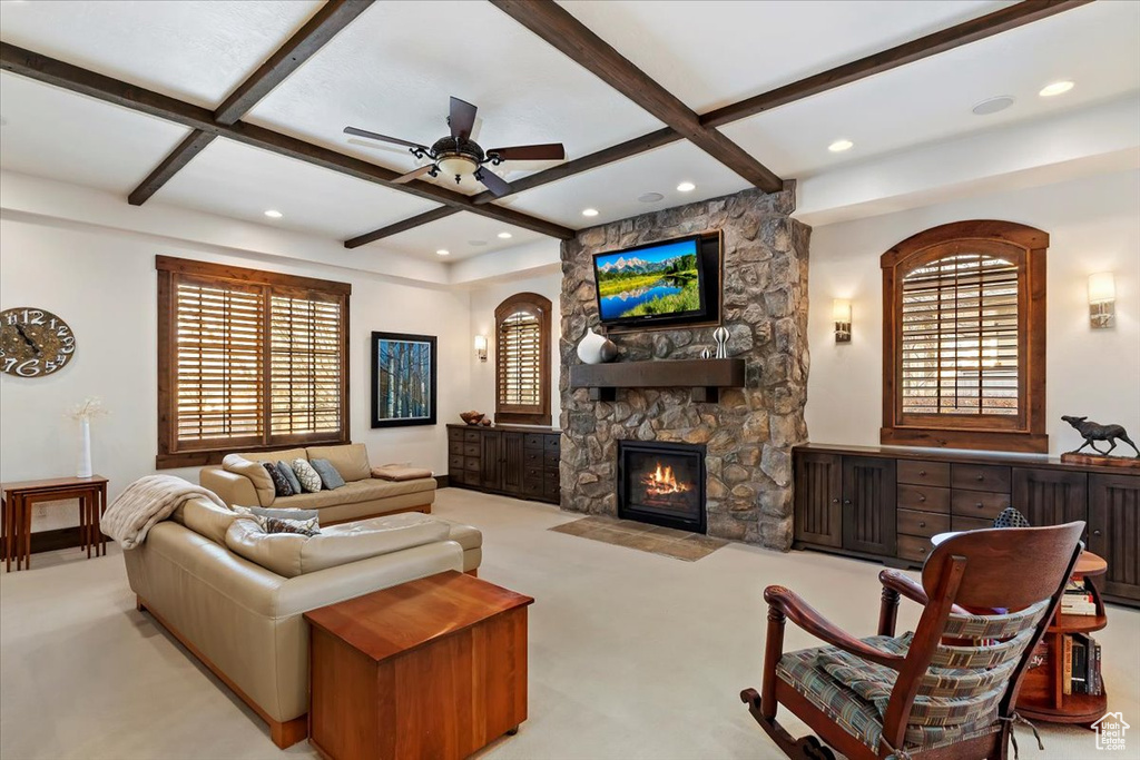 Carpeted living room featuring a stone fireplace, beamed ceiling, a wealth of natural light, and coffered ceiling