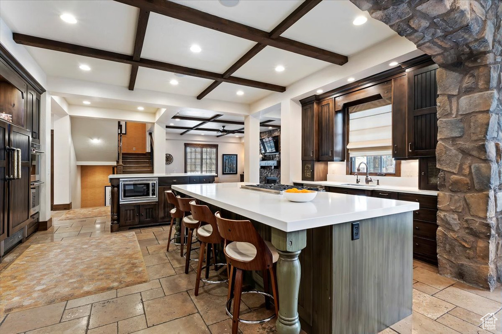 Kitchen with dark brown cabinetry, a kitchen island, coffered ceiling, and appliances with stainless steel finishes