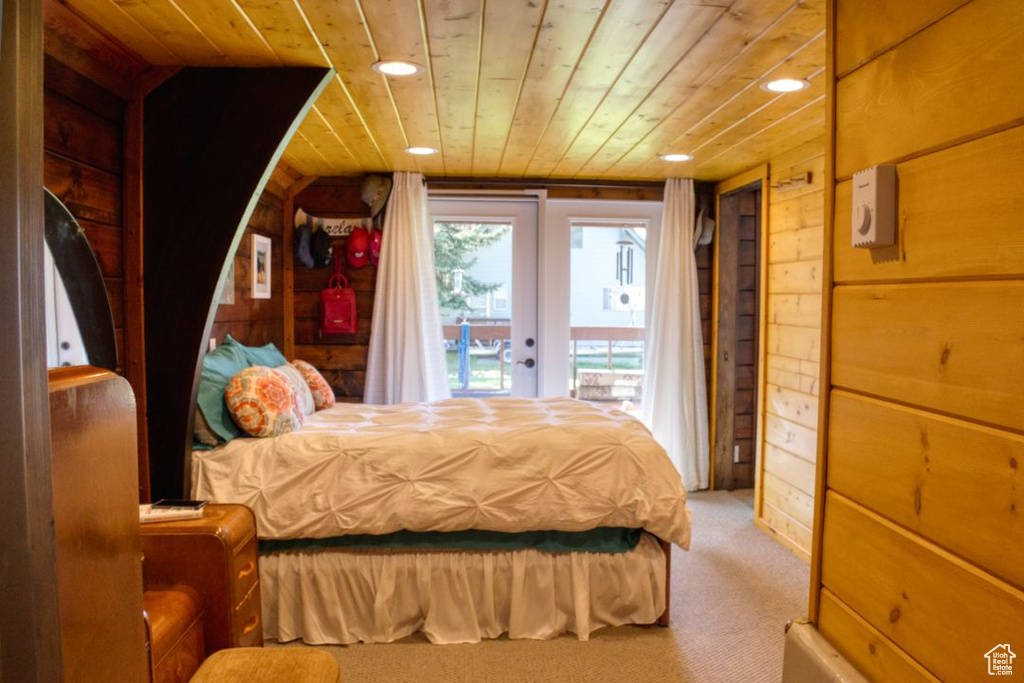 Bedroom with wooden ceiling, wood walls, light colored carpet, and access to exterior