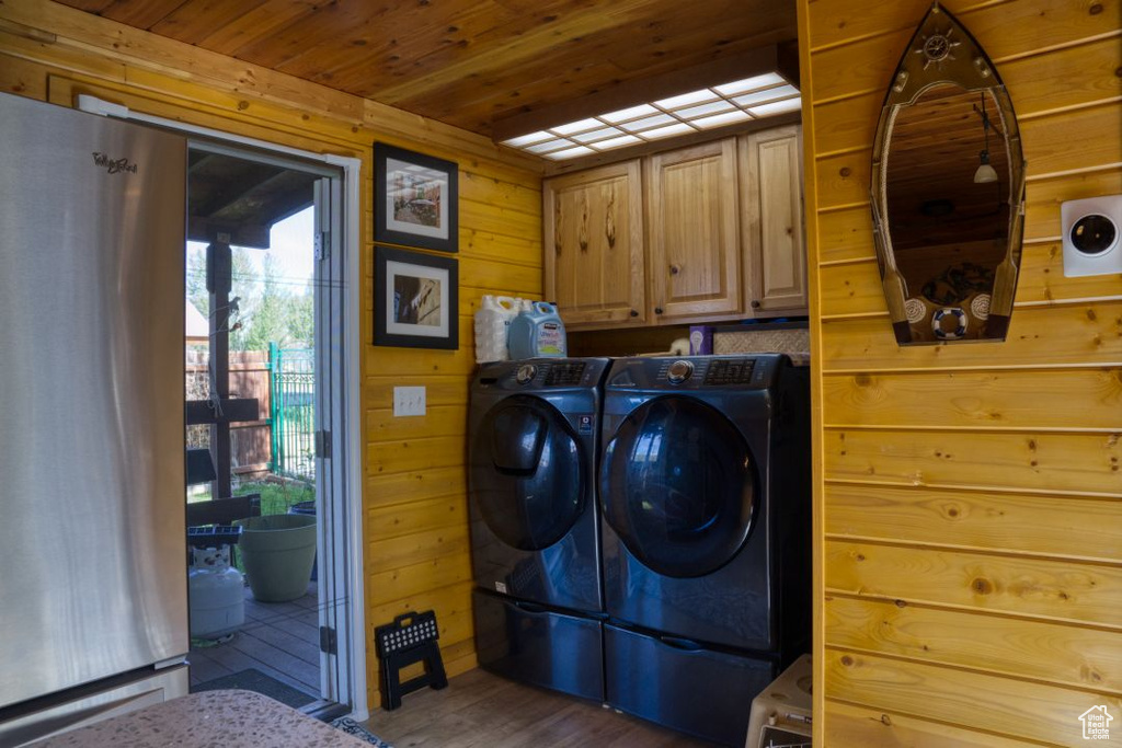 Laundry area featuring wood walls, wood-type flooring, washer and dryer, wood ceiling, and cabinets