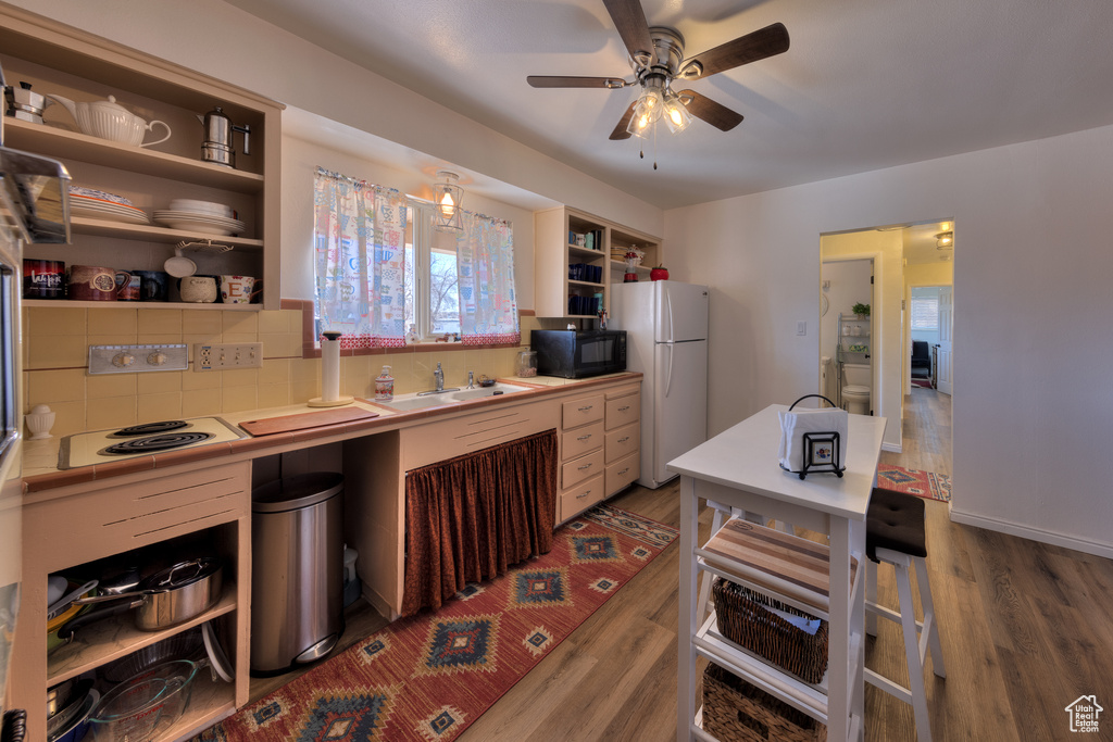 Kitchen featuring backsplash, ceiling fan, dark wood-type flooring, white appliances, and sink