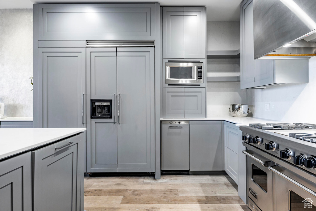 Kitchen with light wood-type flooring, stainless steel appliances, wall chimney exhaust hood, and gray cabinetry