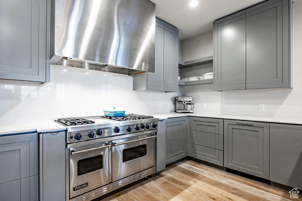 Kitchen with gray cabinets, wall chimney range hood, tasteful backsplash, double oven range, and light wood-type flooring
