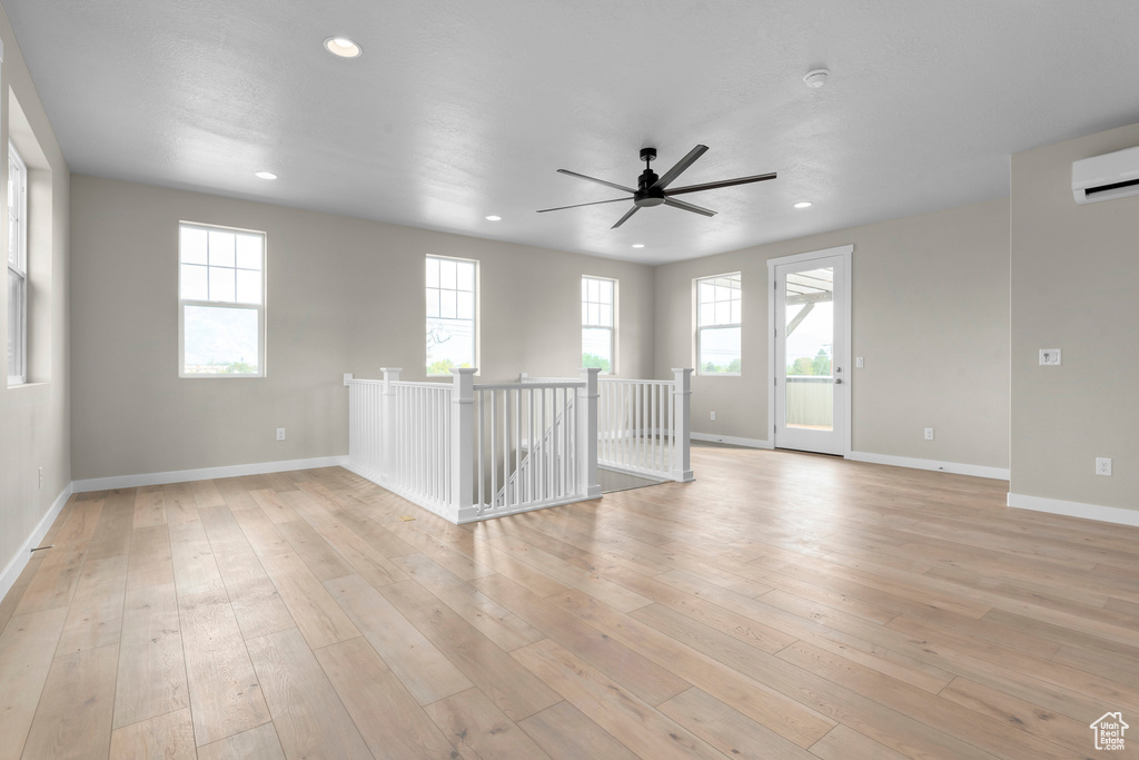 Empty room featuring light hardwood / wood-style flooring, an AC wall unit, and ceiling fan