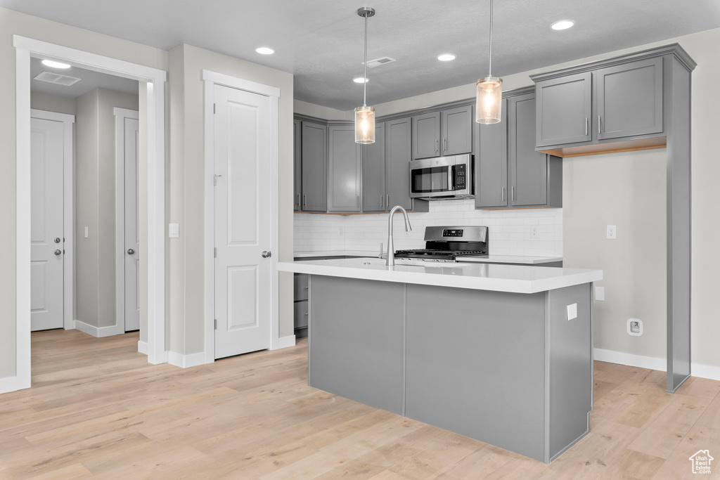 Kitchen with a center island with sink, pendant lighting, gray cabinets, and light hardwood / wood-style flooring