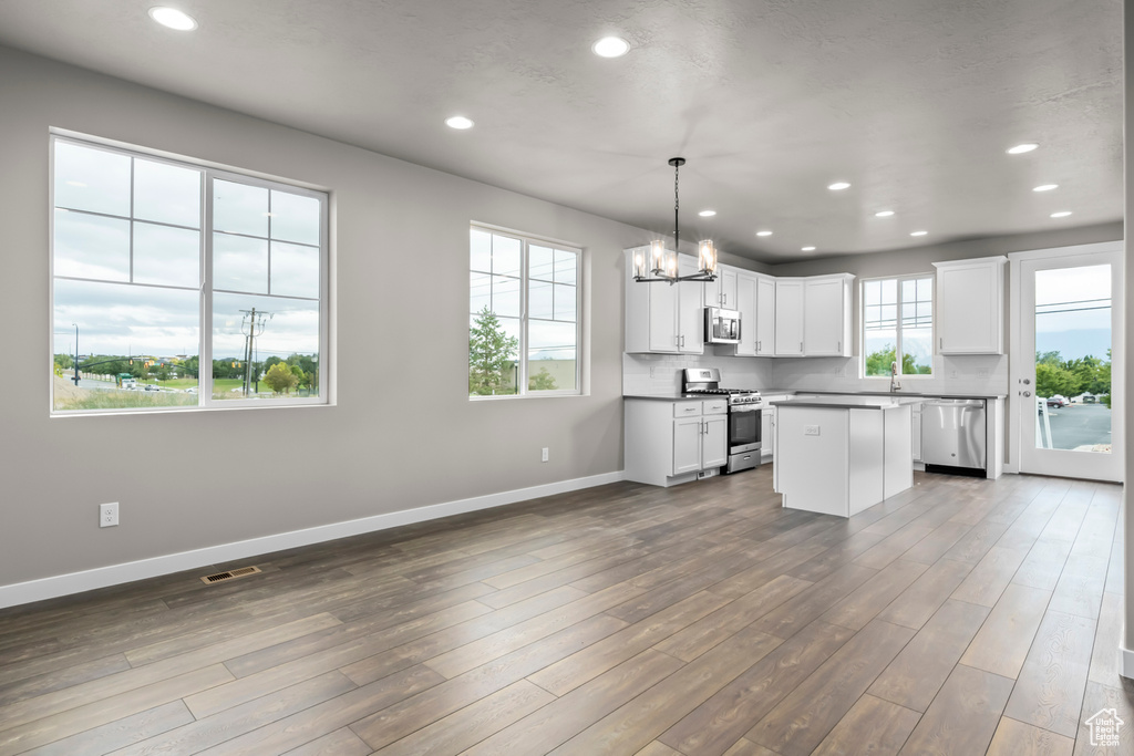 Kitchen featuring a center island, white cabinets, decorative light fixtures, dark hardwood / wood-style flooring, and appliances with stainless steel finishes