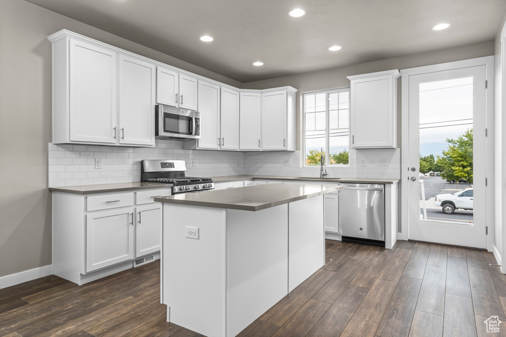 Kitchen featuring a kitchen island, tasteful backsplash, dark wood-type flooring, white cabinets, and stainless steel appliances