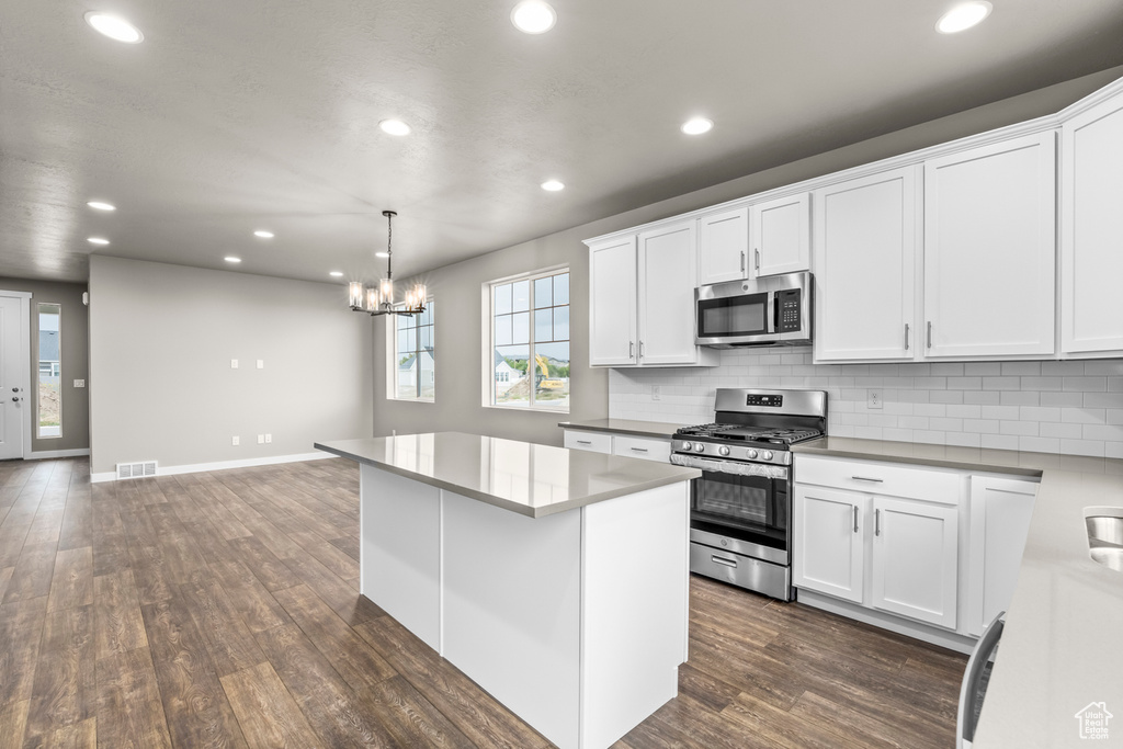 Kitchen featuring dark wood-type flooring, an inviting chandelier, a center island, white cabinetry, and stainless steel appliances