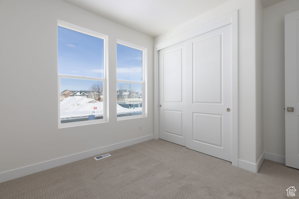 Unfurnished bedroom featuring light colored carpet, a closet, and multiple windows
