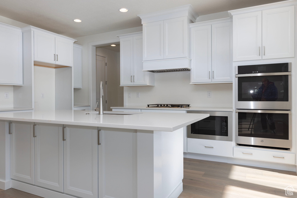 Kitchen featuring double oven, light wood-type flooring, white cabinetry, and black microwave