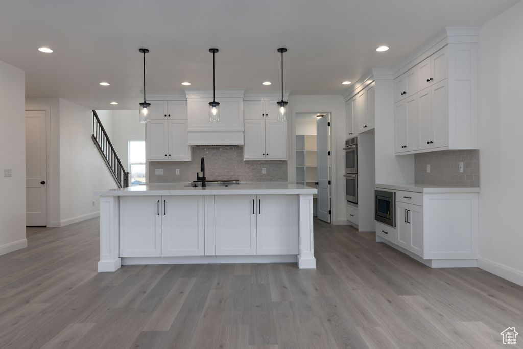 Kitchen with decorative light fixtures, white cabinets, backsplash, and light hardwood / wood-style floors