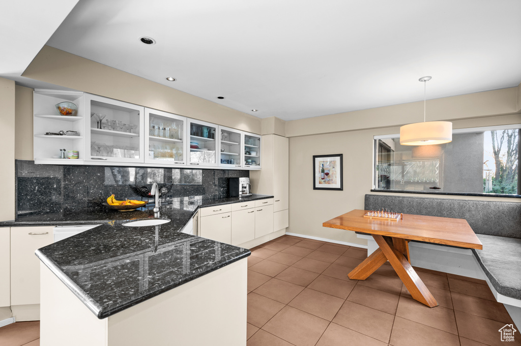 Kitchen featuring light tile flooring, white cabinetry, sink, hanging light fixtures, and backsplash