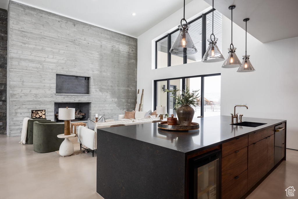 Kitchen featuring concrete floors, sink, a large fireplace, a towering ceiling, and beverage cooler
