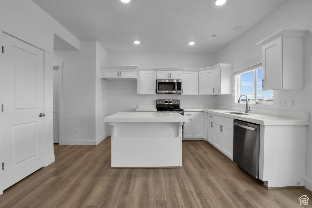 Kitchen featuring appliances with stainless steel finishes, light hardwood / wood-style flooring, a kitchen island, and sink