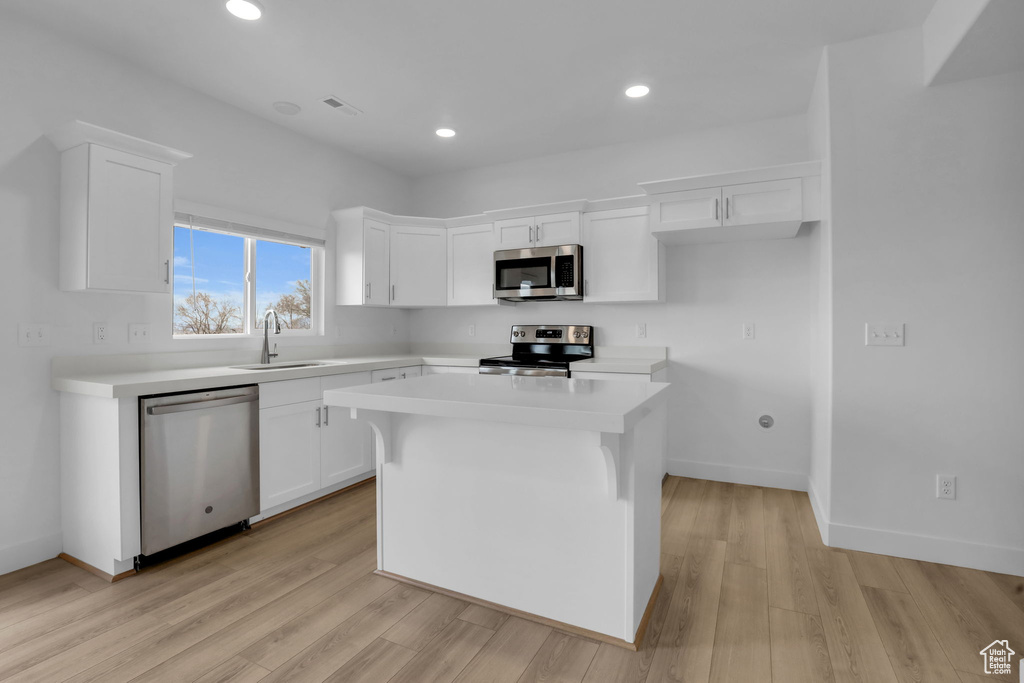 Kitchen with white cabinetry, sink, light hardwood / wood-style floors, a kitchen island, and stainless steel appliances