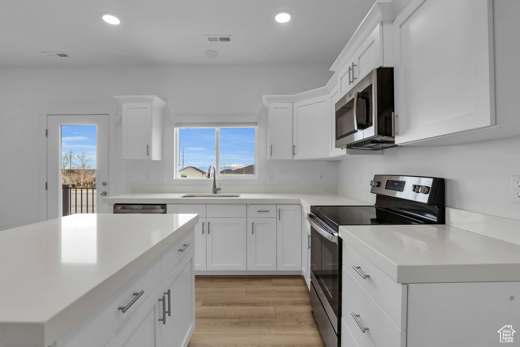 Kitchen featuring stainless steel appliances, sink, white cabinetry, and light hardwood / wood-style floors