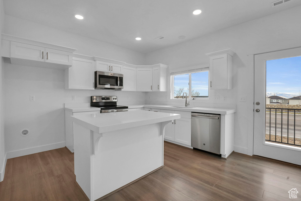 Kitchen featuring dark hardwood / wood-style floors, appliances with stainless steel finishes, white cabinets, and a kitchen island
