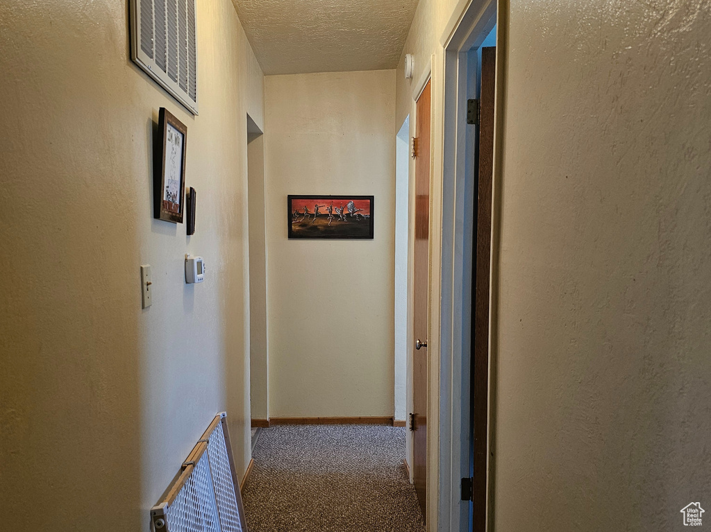 Hall featuring dark colored carpet and a textured ceiling