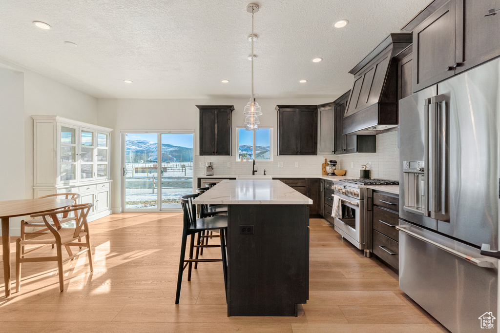 Kitchen with premium range hood, premium appliances, decorative light fixtures, a kitchen island, and light wood-type flooring
