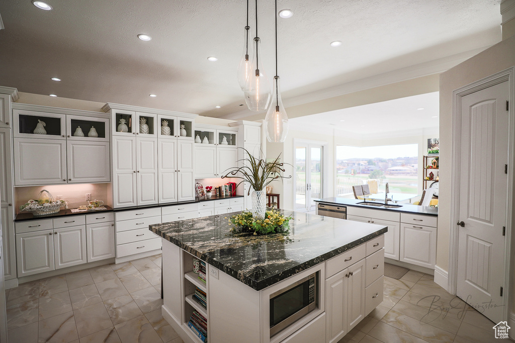 Kitchen with light tile flooring, white cabinets, a kitchen island, and appliances with stainless steel finishes