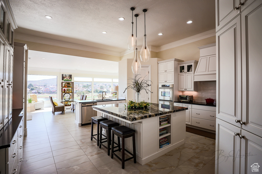 Kitchen with dark stone countertops, a kitchen island with sink, a kitchen breakfast bar, ornamental molding, and stainless steel appliances