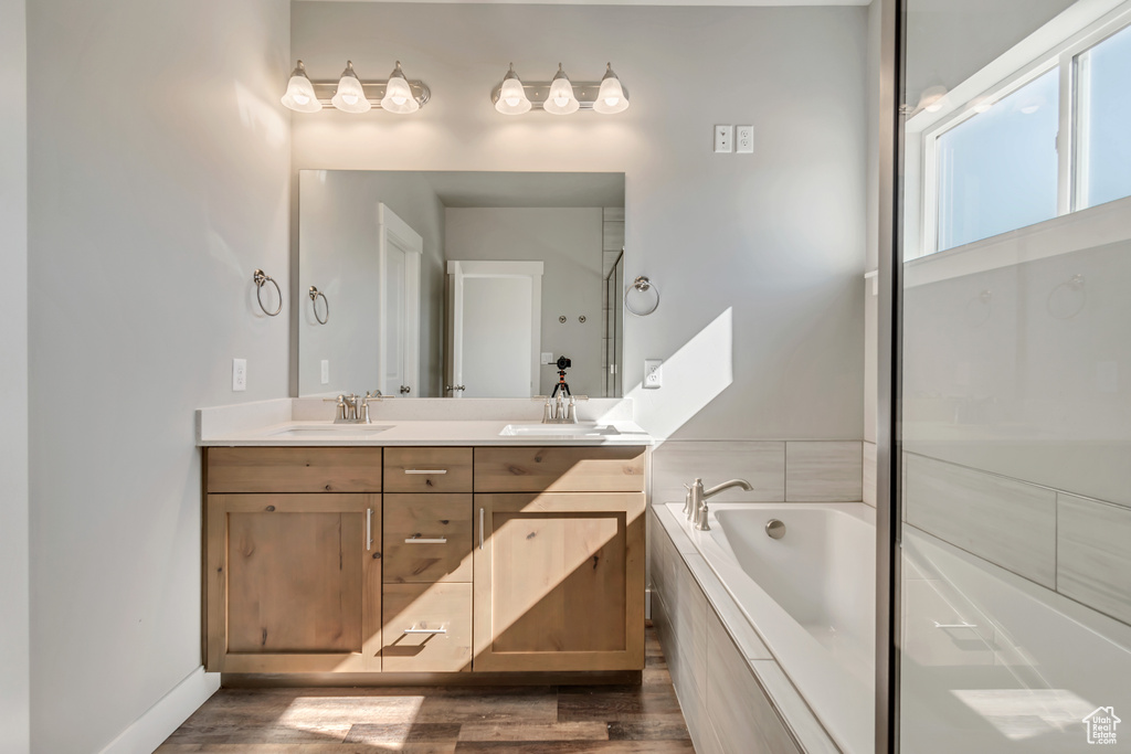 Bathroom featuring hardwood / wood-style flooring, double sink vanity, and a relaxing tiled bath