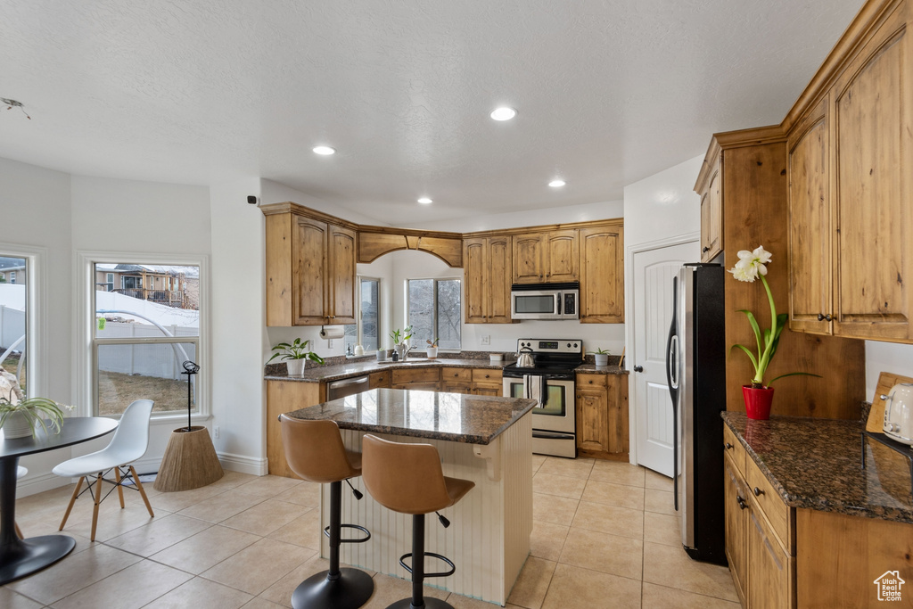Kitchen with a kitchen island, dark stone countertops, light tile floors, a kitchen breakfast bar, and stainless steel appliances
