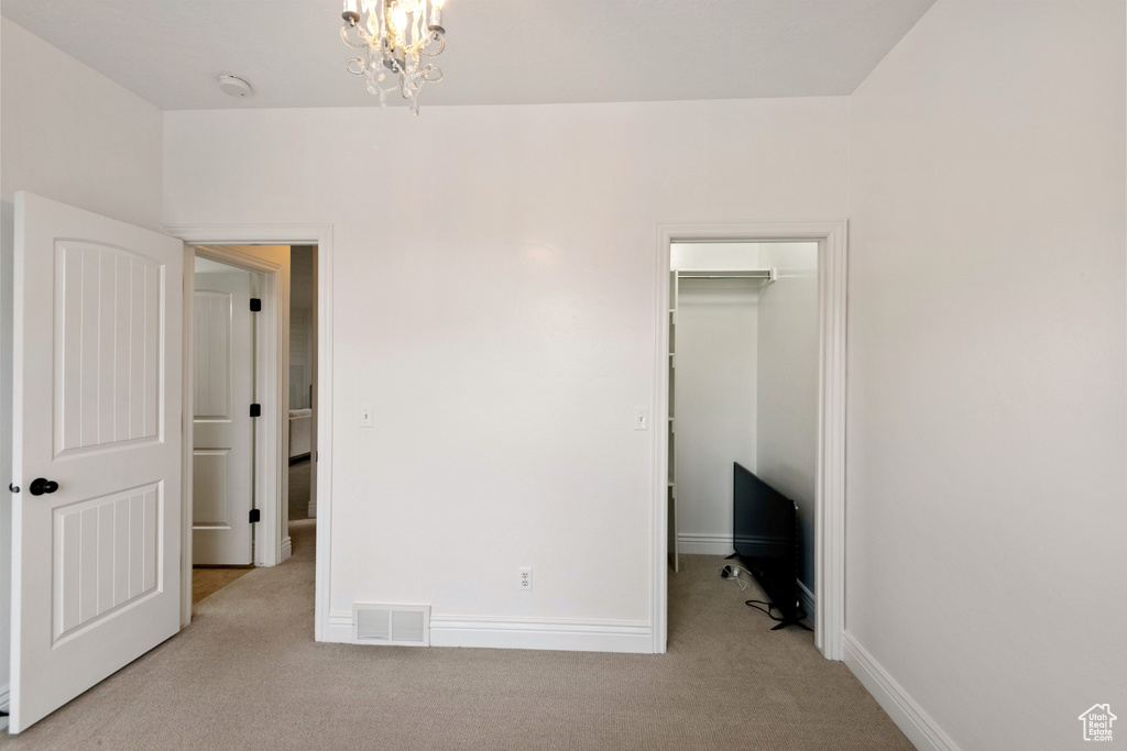 Unfurnished bedroom with a notable chandelier, light colored carpet, a closet, and a spacious closet