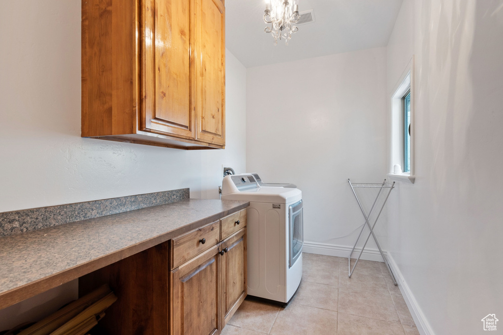 Clothes washing area with cabinets, a chandelier, independent washer and dryer, and light tile floors