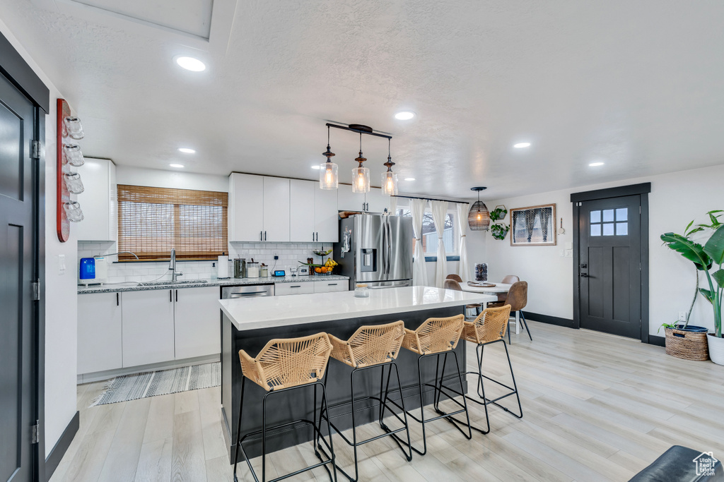 Kitchen with white cabinets, light hardwood / wood-style flooring, a center island, and stainless steel fridge with ice dispenser
