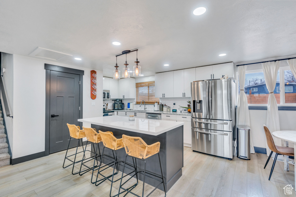 Kitchen with a center island, light hardwood / wood-style flooring, stainless steel appliances, and white cabinets