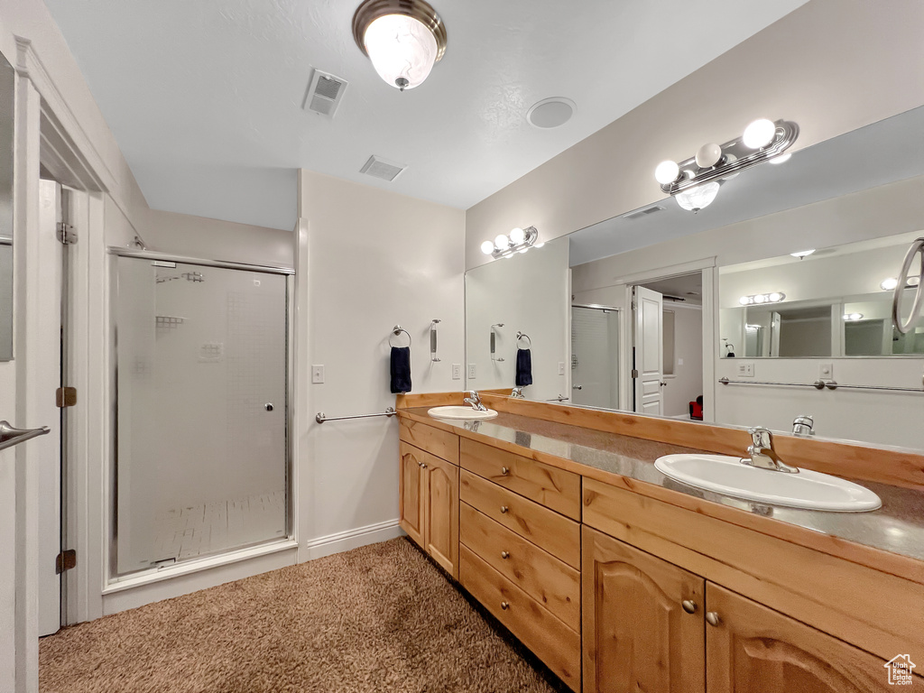 Bathroom with vanity with extensive cabinet space, double sink, and an enclosed shower
