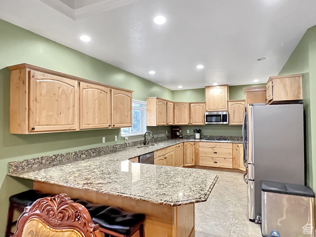 Kitchen with appliances with stainless steel finishes, light brown cabinets, light tile flooring, kitchen peninsula, and a kitchen breakfast bar