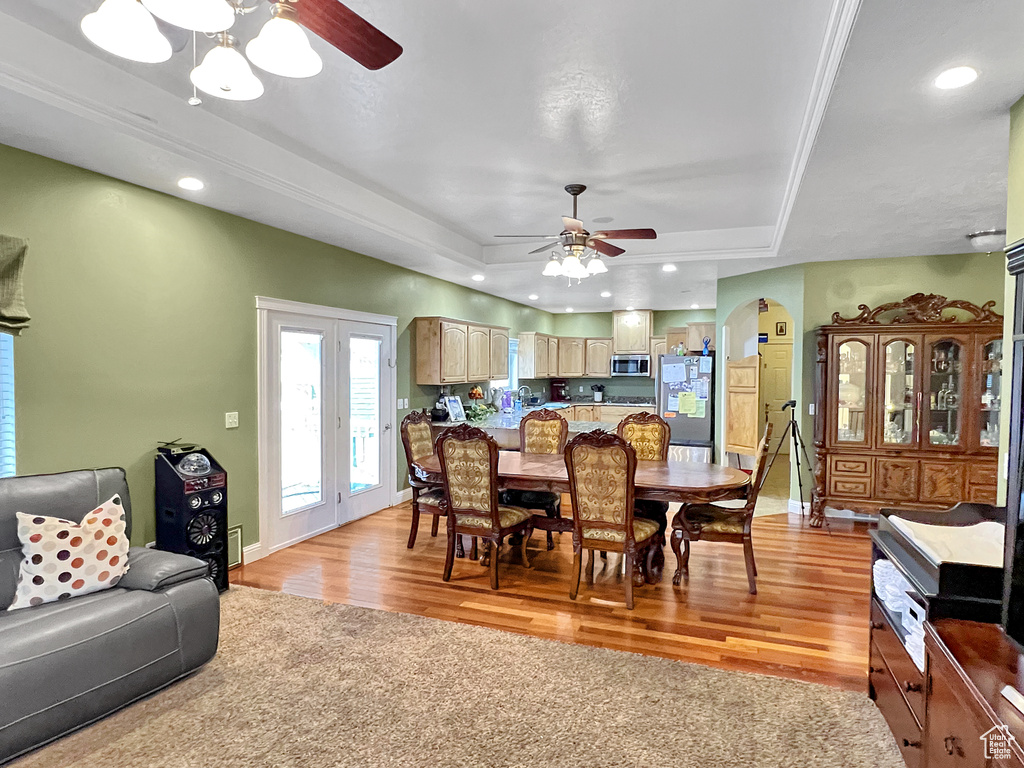 Dining room with light hardwood / wood-style flooring, ceiling fan, and a tray ceiling