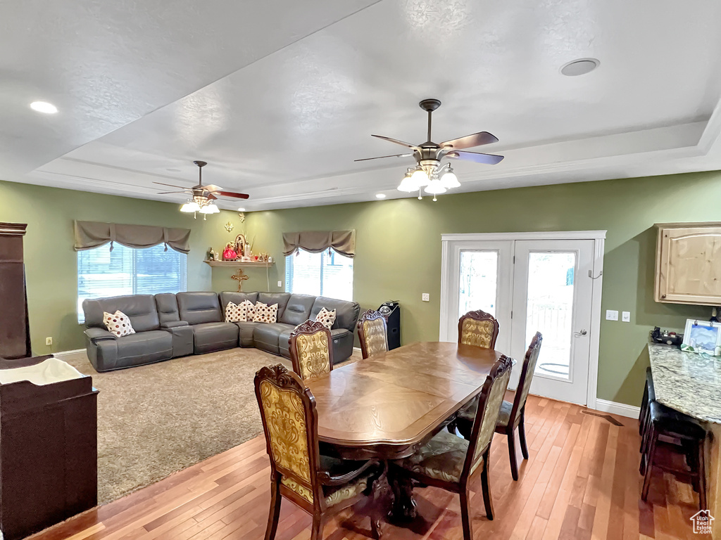 Dining area featuring a tray ceiling, french doors, ceiling fan, and light carpet