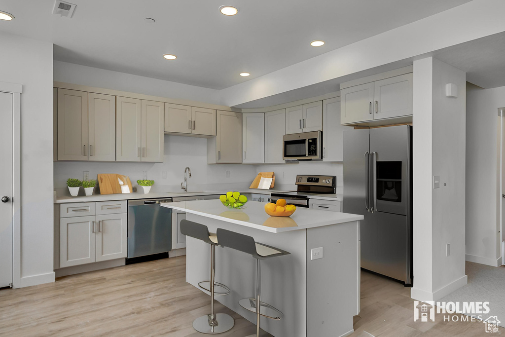 Kitchen with appliances with stainless steel finishes, light hardwood / wood-style floors, sink, a breakfast bar area, and a center island