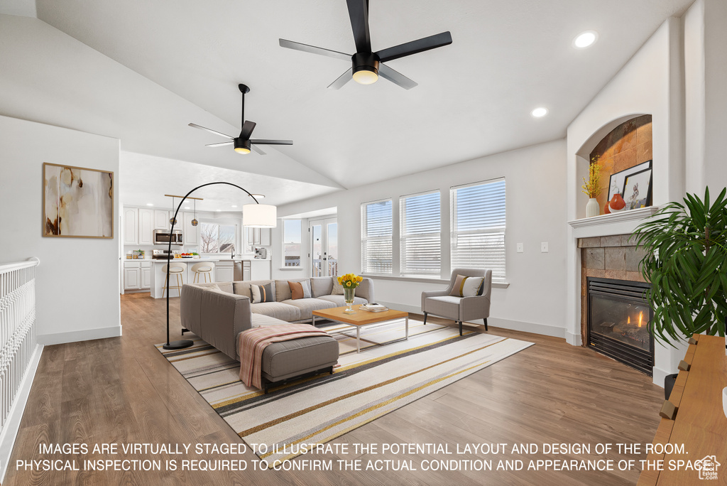 Living room featuring lofted ceiling, a tile fireplace, light hardwood / wood-style flooring, and ceiling fan