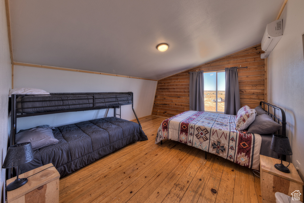 Bedroom featuring an AC wall unit, vaulted ceiling, wood walls, and light hardwood / wood-style flooring