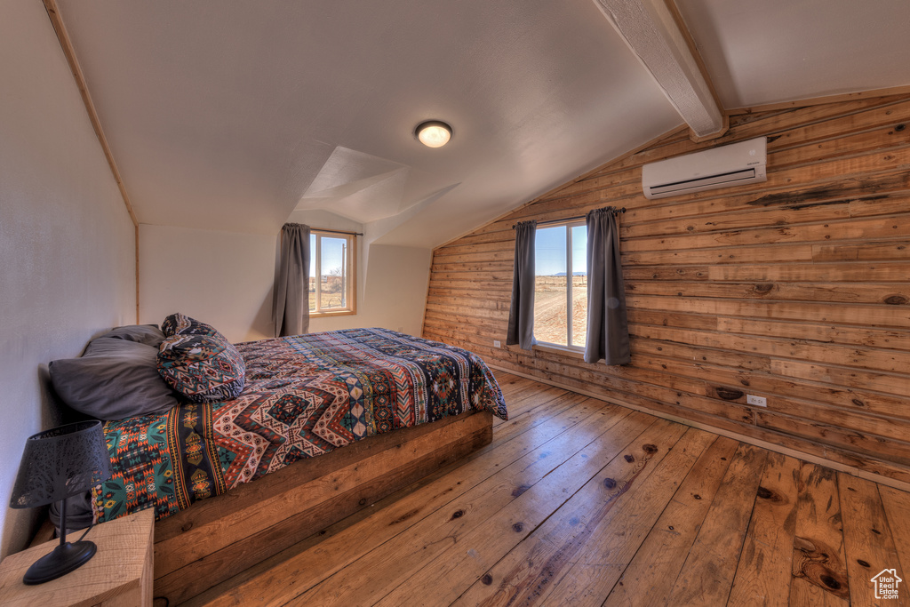 Bedroom featuring a wall mounted air conditioner, lofted ceiling with beams, hardwood / wood-style flooring, and wooden walls