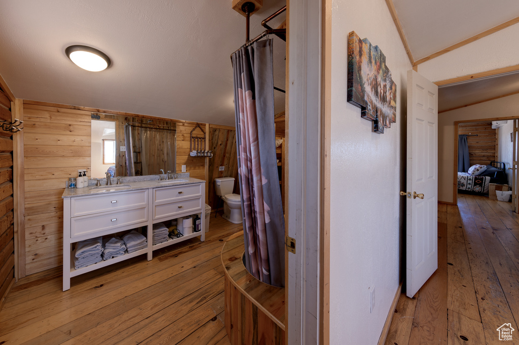 Corridor with vaulted ceiling, wooden walls, light hardwood / wood-style floors, and sink