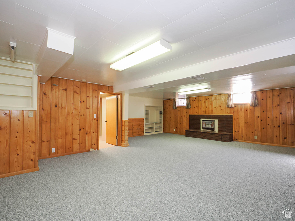 Basement with light colored carpet, wooden walls, and a fireplace