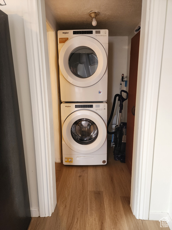 Laundry area with stacked washing maching and dryer and light hardwood / wood-style flooring