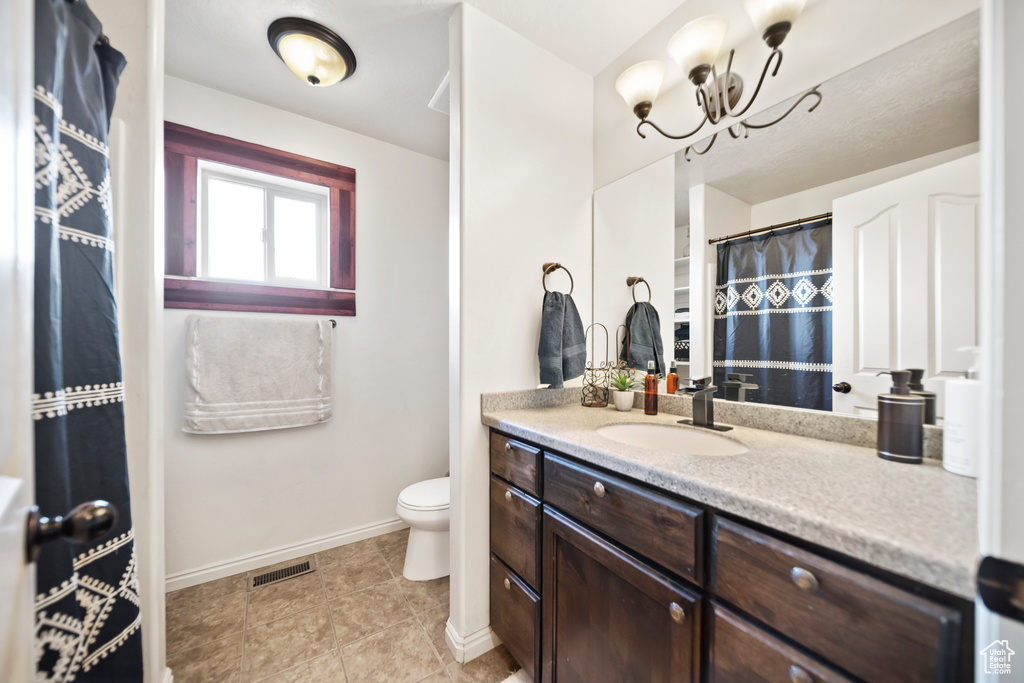 Bathroom with toilet, vanity with extensive cabinet space, tile flooring, and a chandelier