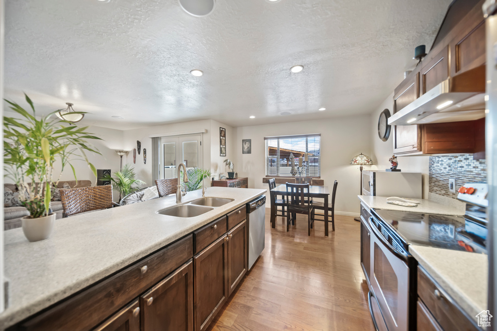 Kitchen with sink, a textured ceiling, dishwasher, light hardwood / wood-style floors, and range with electric stovetop
