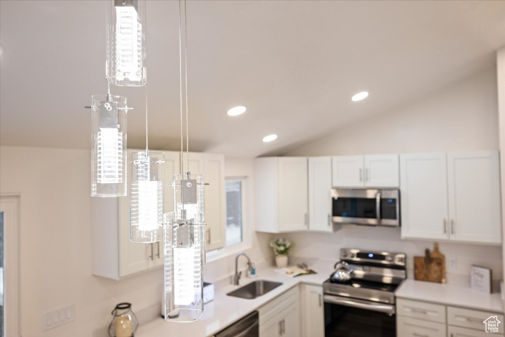 Kitchen with appliances with stainless steel finishes, white cabinets, sink, lofted ceiling, and pendant lighting