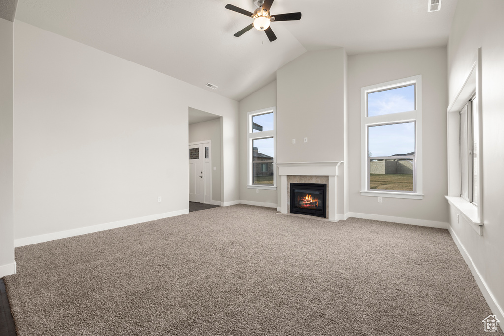Unfurnished living room featuring a wealth of natural light, high vaulted ceiling, ceiling fan, and carpet