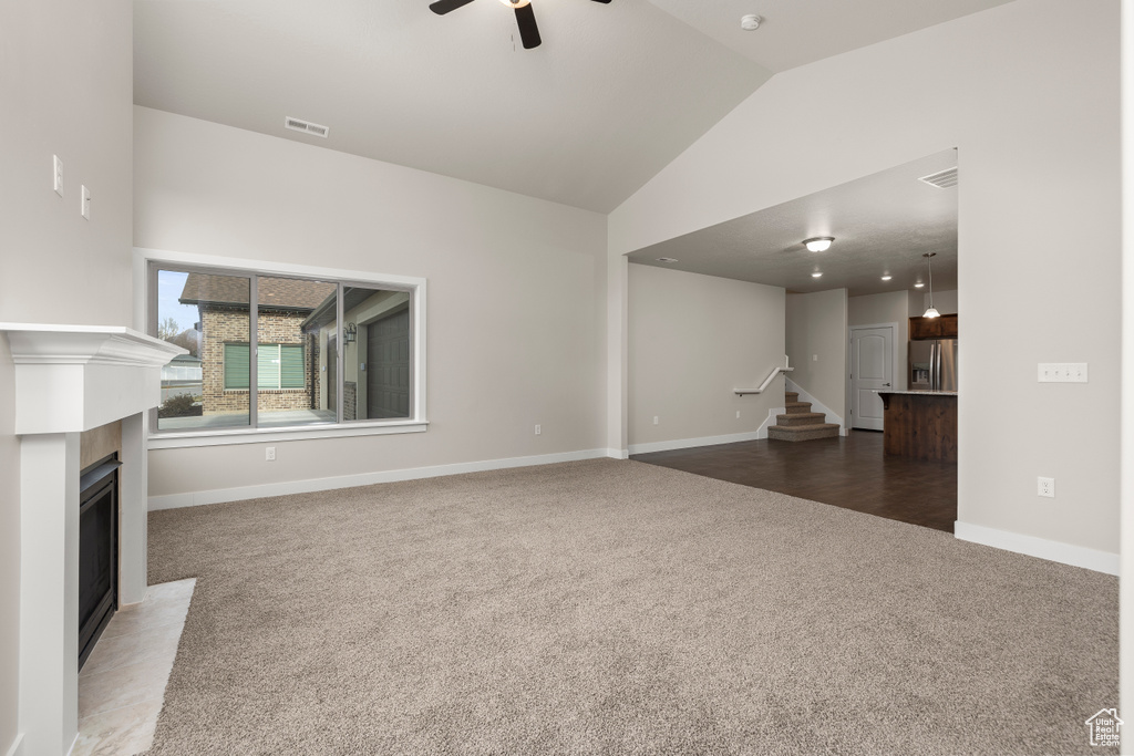 Unfurnished living room featuring vaulted ceiling, dark colored carpet, and ceiling fan
