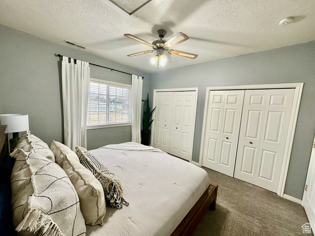 Bedroom with multiple closets, a textured ceiling, dark carpet, and ceiling fan
