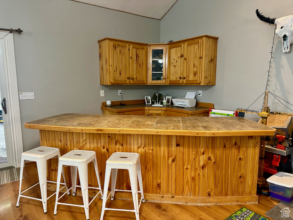 Kitchen featuring vaulted ceiling, kitchen peninsula, light hardwood / wood-style floors, and a kitchen breakfast bar