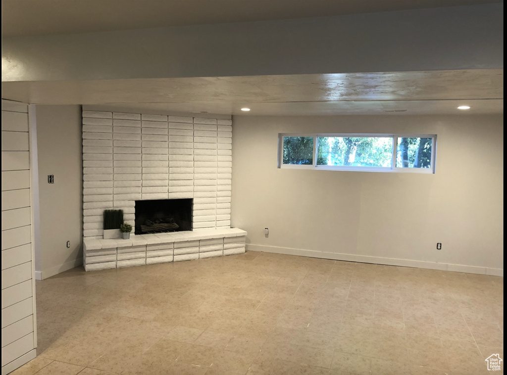 Unfurnished living room featuring brick wall, a fireplace, and light tile flooring